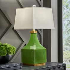 a green lamp sitting on top of a table next to a book and potted plant