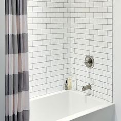 a bathtub with shower curtain and white tile walls in a small bathroom, next to a window