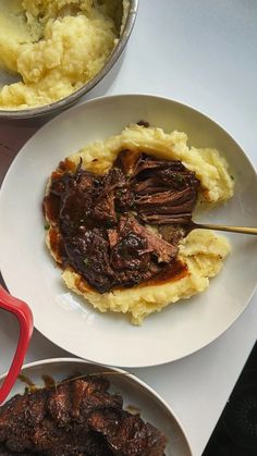 two plates with meat, mashed potatoes and gravy next to a pot of mashed potatoes