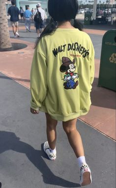 a woman walking down the street wearing a yellow sweatshirt that says walt disney's