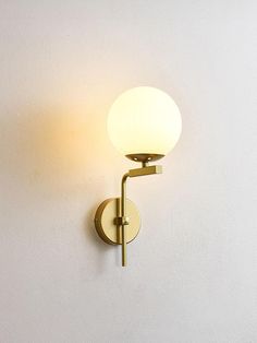 a wall mounted light on the side of a white wall with a round glass shade