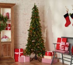 a christmas tree with presents in front of it next to a chair and brick wall