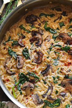 pasta with mushrooms and spinach in a pan on a table next to utensils