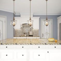 a large kitchen with marble counter tops and white cabinets, along with two chandeliers hanging from the ceiling