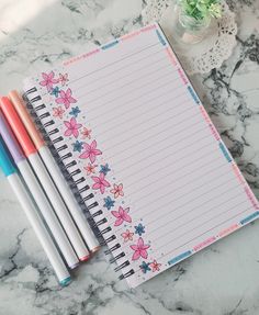 three pencils are sitting on top of a notepad next to two pens and a potted plant