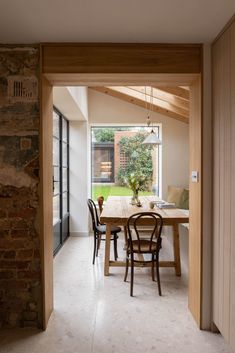 a dining room table and chairs in front of a brick wall with an open door