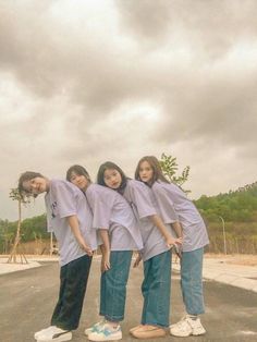 four people standing in the middle of an empty parking lot wearing purple shirts and blue jeans