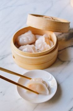 dumplings and chopsticks sit on a white plate next to a wooden box