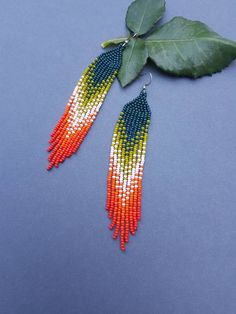 two pairs of colorful beaded earrings with green leaves on the bottom and blue background