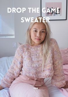 a young woman sitting on top of a bed wearing pink pants and a knitted sweater