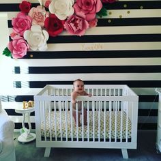 a baby sitting in a white crib next to a wall with flowers on it