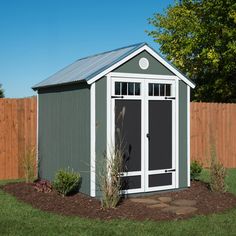 a small gray shed sitting in the middle of a yard next to a wooden fence