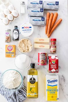 ingredients to make carrot cake laid out on a marble counter top, including eggs, flour, butter, and other items