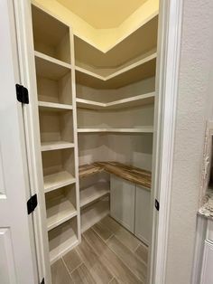 an empty walk - in closet with white shelves and wood flooring on the walls