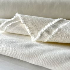 two white linens folded on top of each other with fraying at the edges