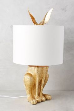 a golden cat lamp with a white shade on it's head and tail sitting next to a gray wall