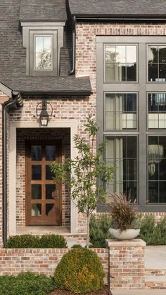 a brick house with large windows and plants in the front yard