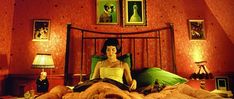 a woman sitting on top of a bed in a room with red walls and pictures above it