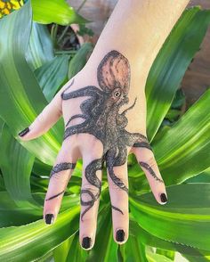 a hand with an octopus tattoo on it and green leaves in the foreground, next to a yellow flower