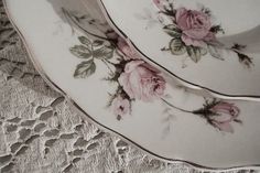 two plates with pink roses on them sitting on a lace doily covered tablecloth