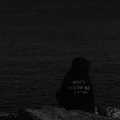 a person sitting on top of a rock near the ocean under a full moon sky