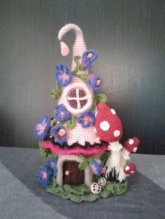 a crocheted house with mushrooms and flowers on the roof is shown in front of a gray background