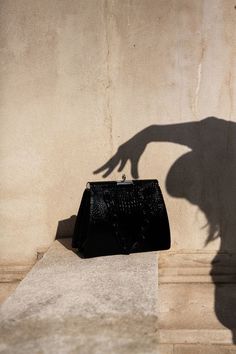 the shadow of a woman's hand holding onto a black purse next to a wall