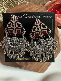 Description of the Earrings:   This is an exquisite contemporary twist on traditional craftsmanship on mashru silk Ajrakh handblock fabric earrings. This is absolutely perfect for the contemporary fashion enthusiast but with a fresh take on ethnic wear.  There are many variations of this design.  Design: Handcrafted piece in a rich mashru silk or handloom cotton handblock Ajrakh pattern fabric base  with a contrasting set of oxidized gunghroo embellishments along the bottom of the earrings. This is a unique Chandbali design.  Each piece showcases the craftsmanship and unique and clean finish, giving it a bespoke touch that celebrates the skill of our artisans Highlights of the piece: ** Length of the earrings: 2.25 inches, including the gunghoroo height. ** Free shipping over $35 The measu Bohemian Dual-tone Danglers For Gift, Bohemian Dual-tone Earrings As Gift, Black Bohemian Danglers For Festivals, Bohemian Oxidized Jhumkas As Gift, Bohemian Oxidized Jhumkas For Gift, Handmade Temple Jewelry Danglers For Festival, Bohemian Danglers For Navratri Gift, Bohemian Black Jhumkas For Festive Occasions, Bohemian Black Danglers For Gift