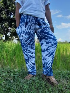 a person standing in the grass wearing blue and white tie - dyed pants with trees in the background