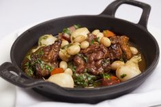 a skillet filled with meat and vegetables on top of a white table next to a napkin