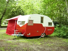 a red and white trailer is parked in the grass next to some trees with an awning over it