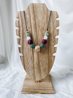 a wooden necklace on a stand with white and purple beads hanging from it's sides