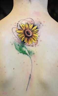 a sunflower tattoo on the back of a woman's upper back, with green splots