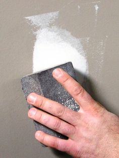 a hand holding a sponge over a gray wall with white paint on the top and bottom