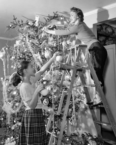 two women are decorating a christmas tree in the living room with their ladders