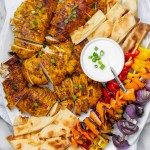 a platter with chicken skewers, vegetables and pita bread