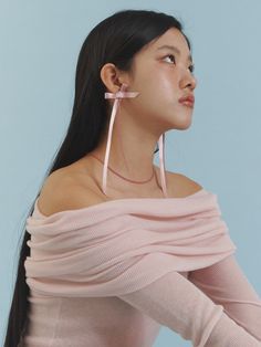 a woman with long black hair wearing a pink sweater and earrings, looking up at the sky