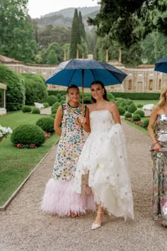 three women are standing under umbrellas in the rain at a formal event, one woman is holding an umbrella