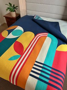 a bed covered in a colorful quilt next to a nightstand with a potted plant