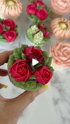 cupcakes decorated with pink and red flowers are being held by a woman's hand