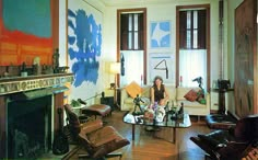 a woman sitting on a couch in a living room with two windows and a fireplace