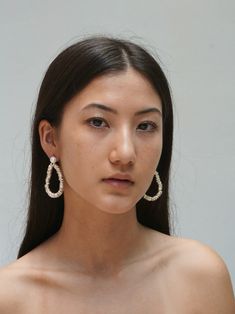 a woman with long dark hair wearing large white earrings and a strapless top is looking at the camera