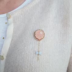 a close up of a person wearing a sweater and holding a brooch with a chain attached to it