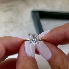 a woman's hand holding an engagement ring with a diamond in front of her