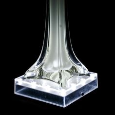 a clear glass vase sitting on top of a black surface with lights around it's base