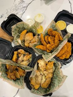 four takeout containers filled with fried chicken and dipping sauces on a marble countertop