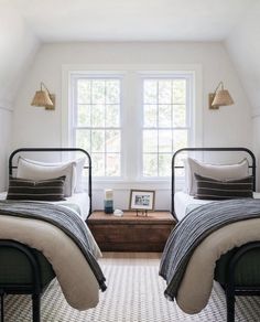 two twin beds in a bedroom with white walls and carpeted flooring next to windows