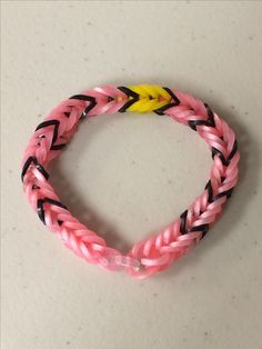 a pink and black braided bracelet with a yellow button on the end is sitting on a white surface