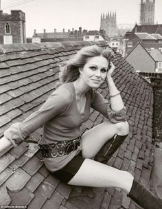 a woman sitting on top of a roof next to a tall building with a clock tower in the background