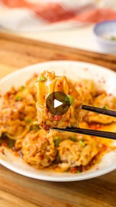 a white plate topped with pasta and meat covered in sauce, being held by two black chopsticks